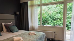 Quarto de hotel com cama, radiador e janela com vista para o verde.