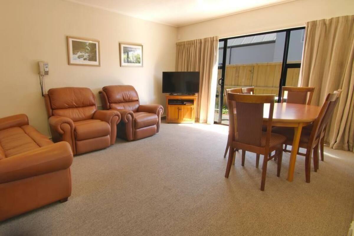 Ein Wohnzimmer mit einer Sofagarnitur, einem Fernseher und einem Essbereich mit Stühlen und einem Tisch.