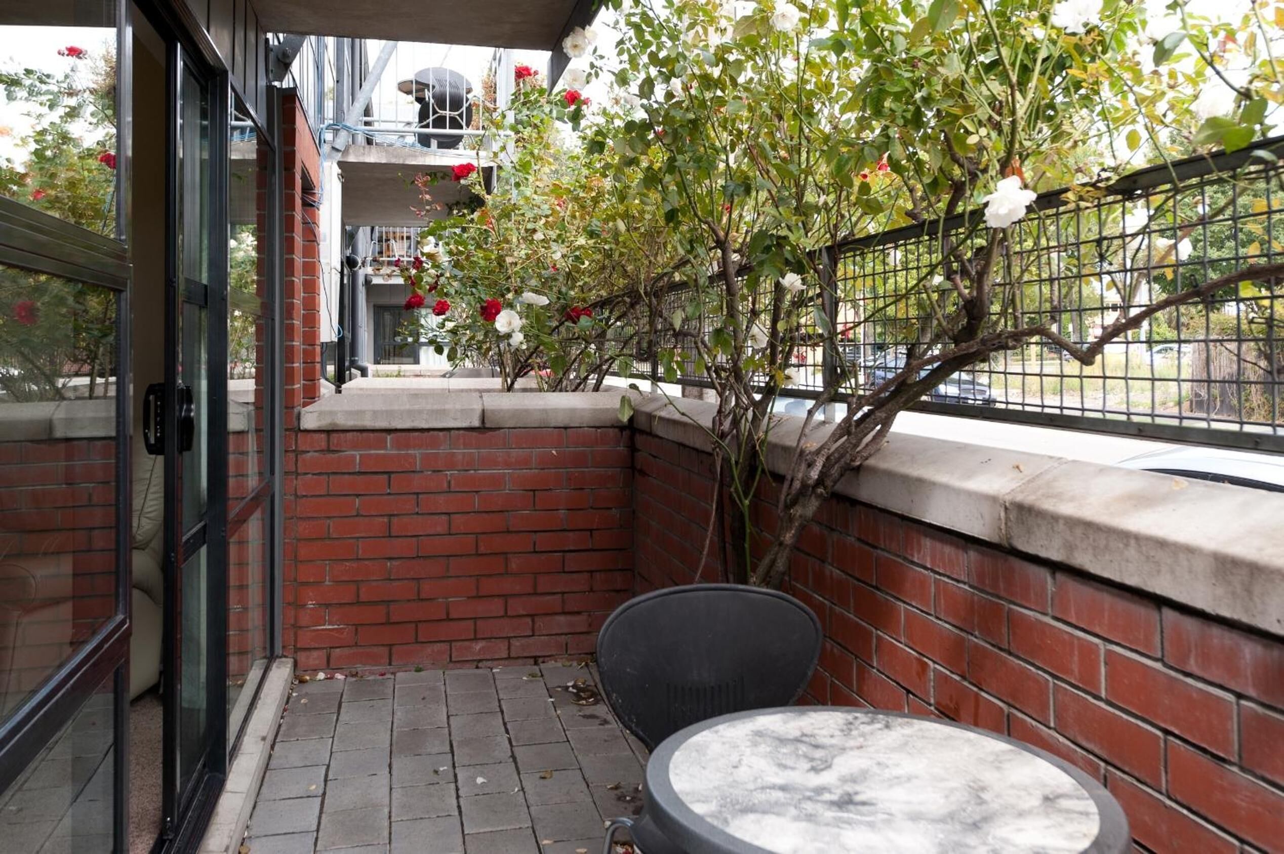 Un pequeño patio al aire libre con un muro de ladrillo, un puerta de vidrio y una mesa redonda.