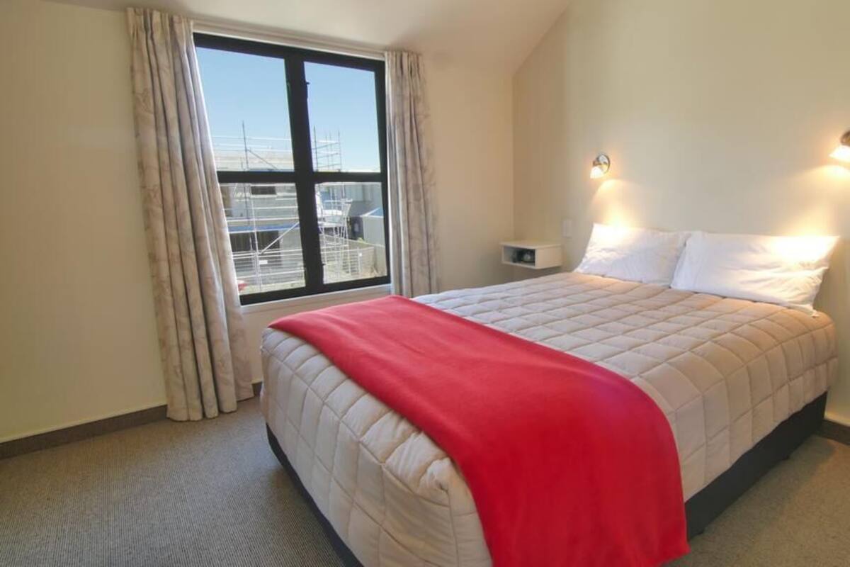 Ein Hotelzimmer mit Bett, einem Fenster mit Vorhängen, einem Nachttisch und einer Wandleuchte.