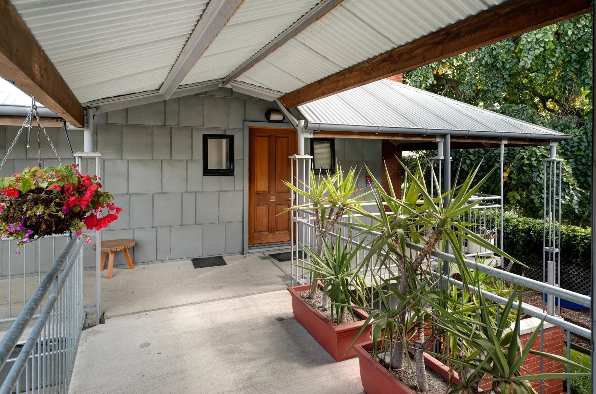 A covered porch with a wooden bench, potted plants, and a metal railing.