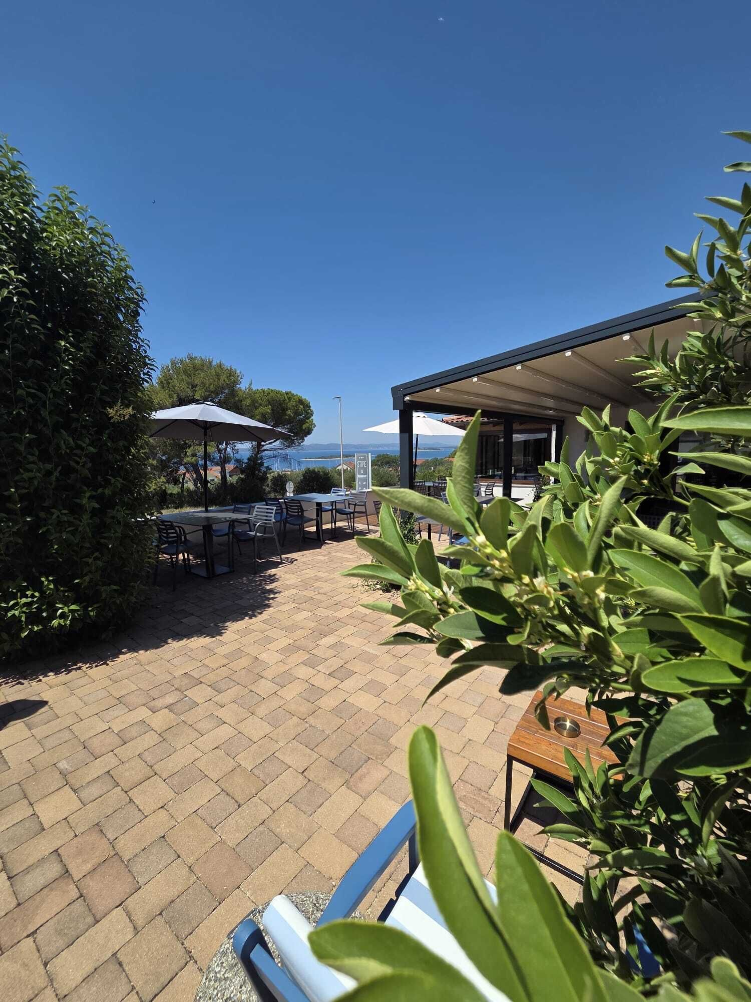An outdoor seating area with tables and chairs, a covered patio, and a view of the sea.