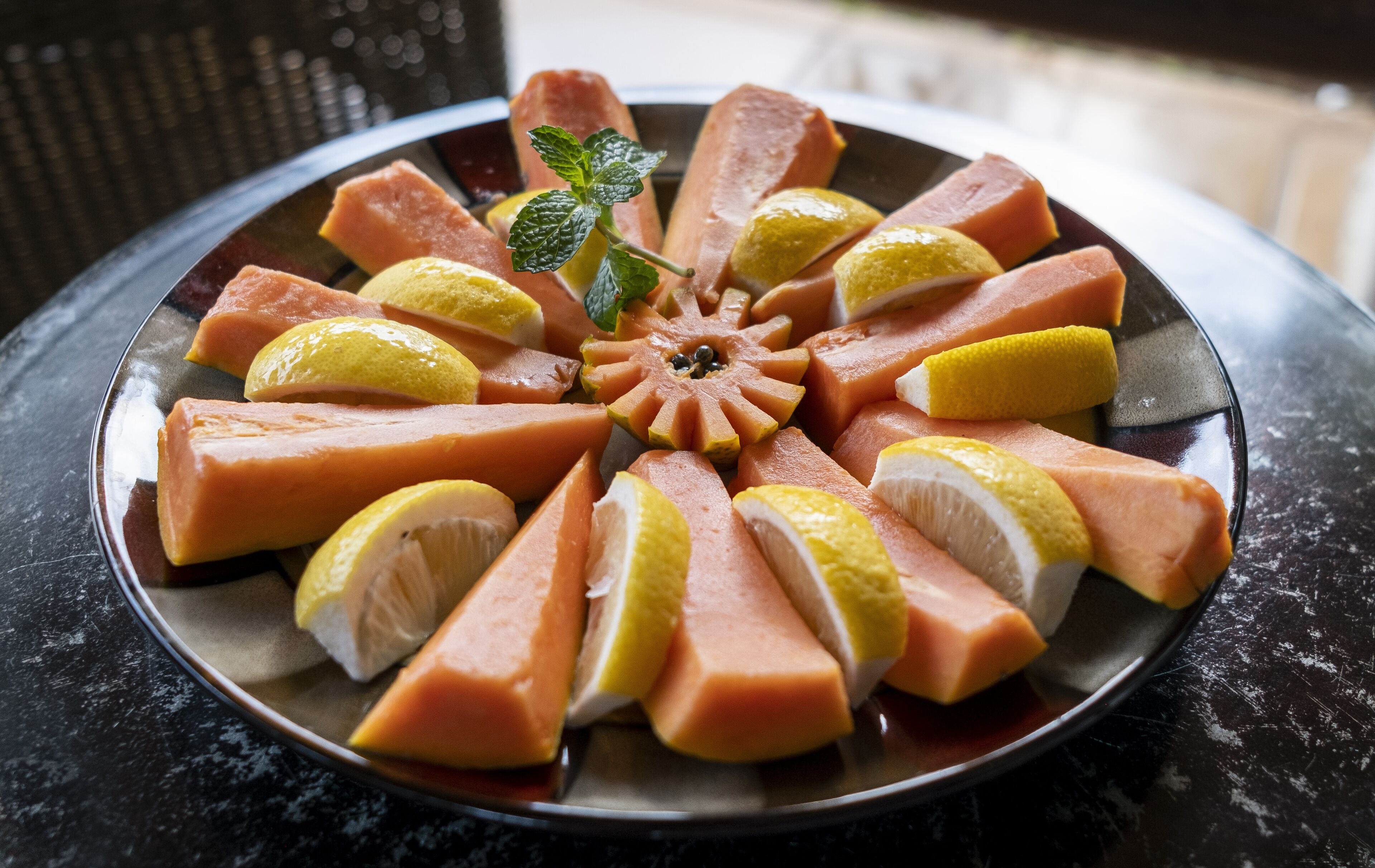 A plate of sliced fruits and vegetables arranged in a circular pattern on a dark surface.