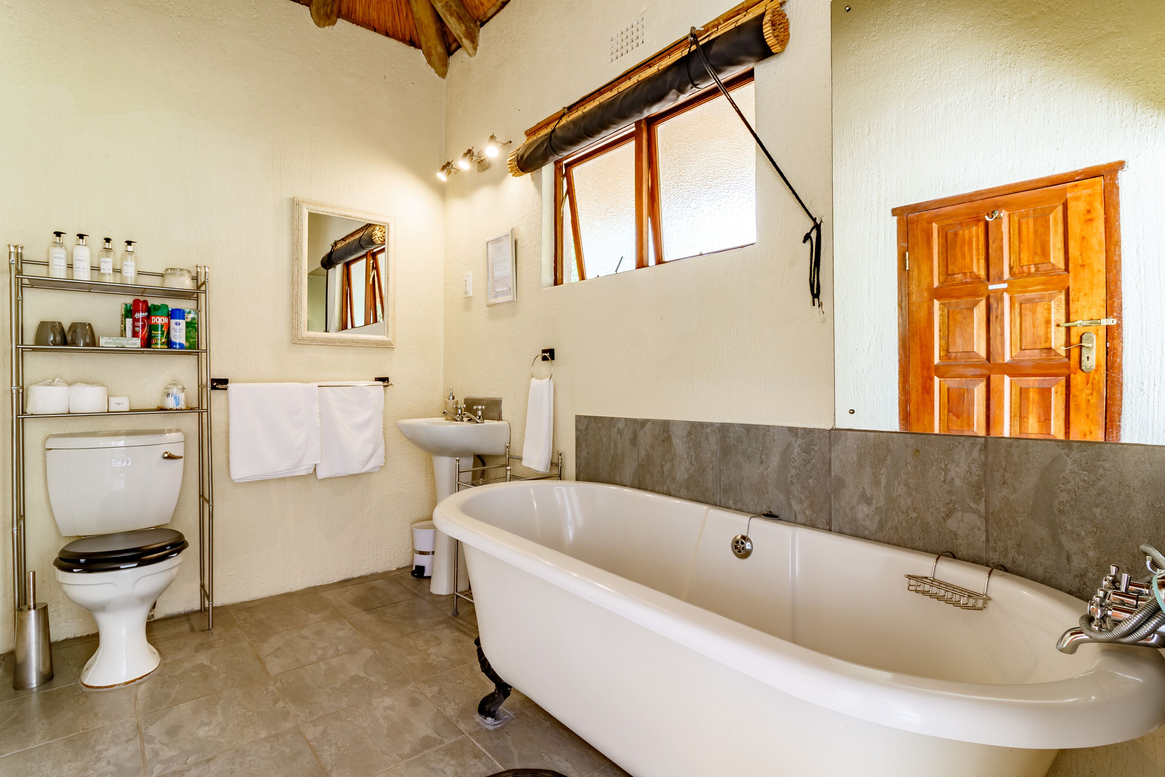 A bathroom with a freestanding bathtub, toilet, and shelves with toiletries.
