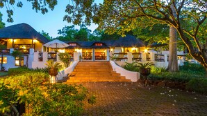 A resort with a thatched-roof building, a paved entrance, and lush greenery.