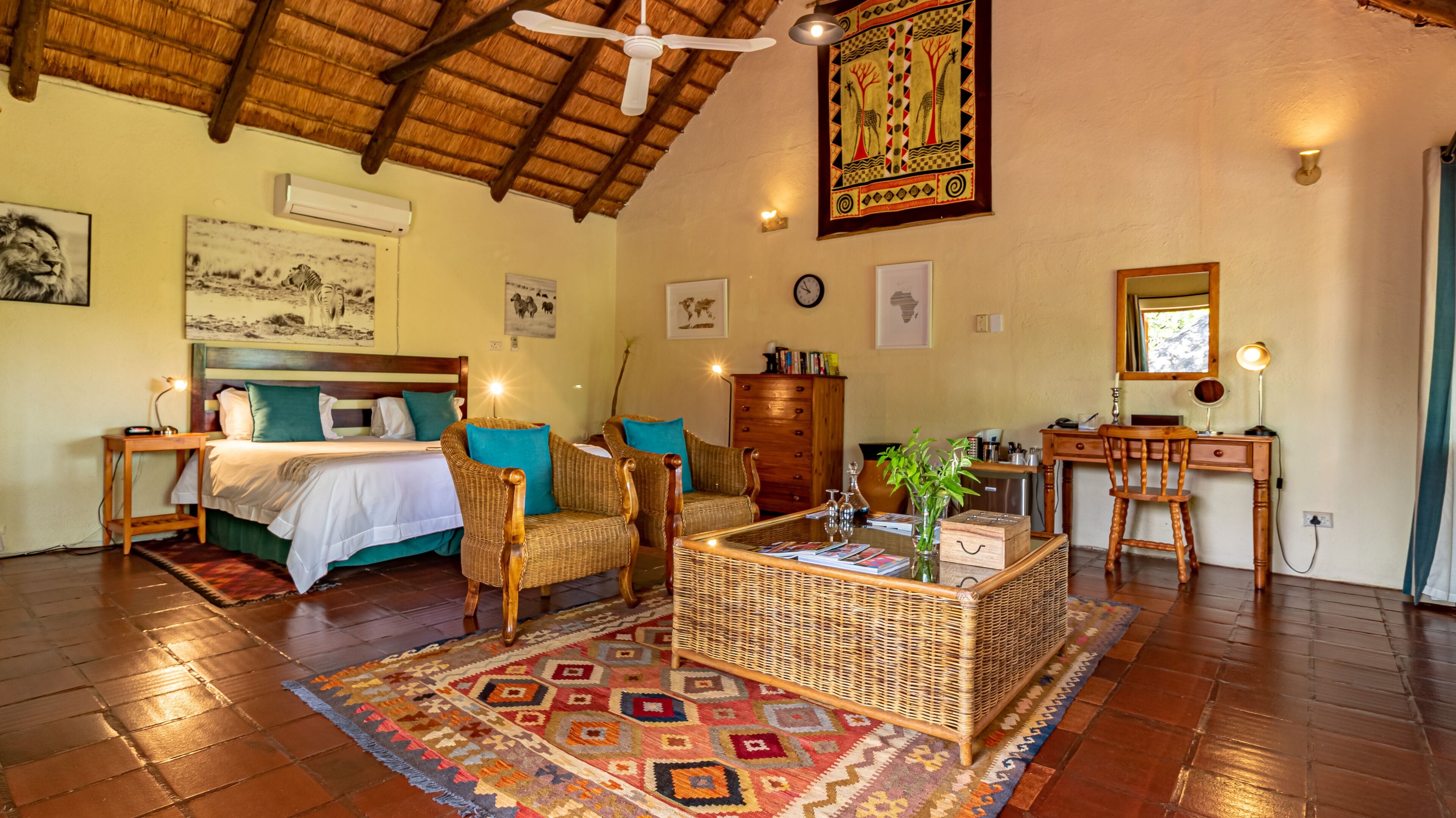 A spacious room with a bed, two wicker chairs, a coffee table, a desk, and a large decorative tapestry.