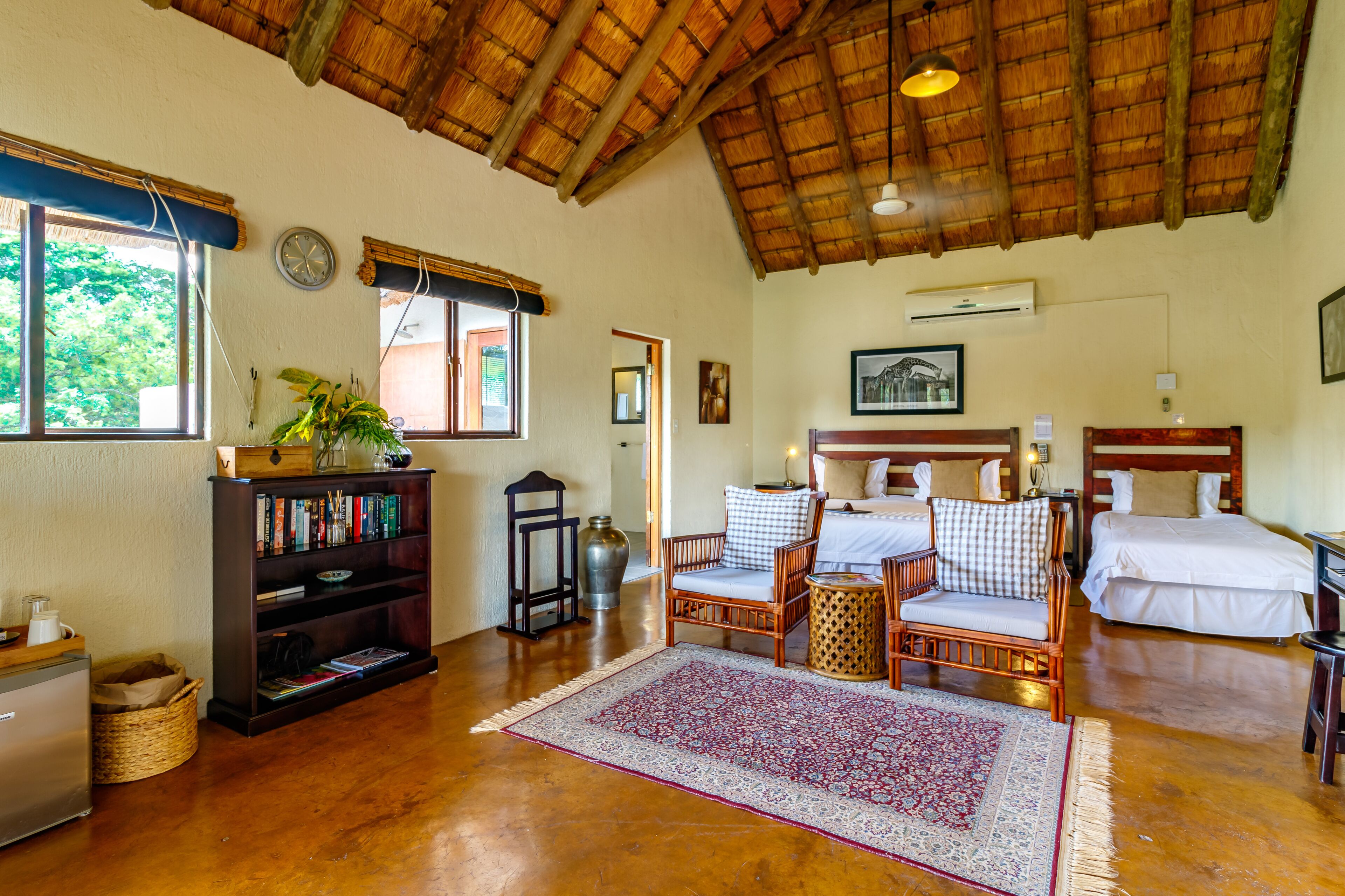 A spacious room with a wooden ceiling, a large window, a bookshelf, a bed, and a small table.