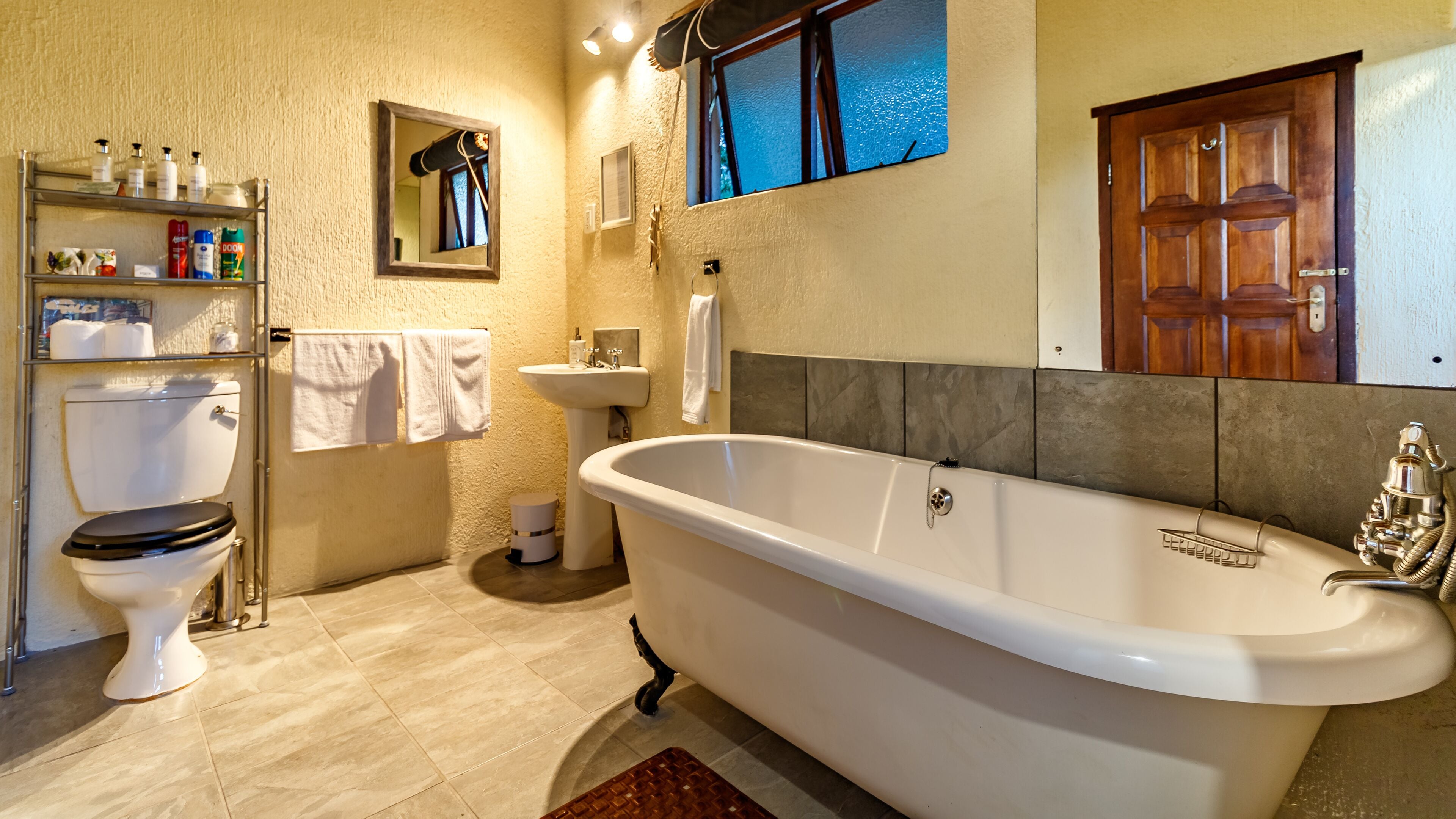 A bathroom with a bathtub, toilet, sink, and shelves with toiletries.