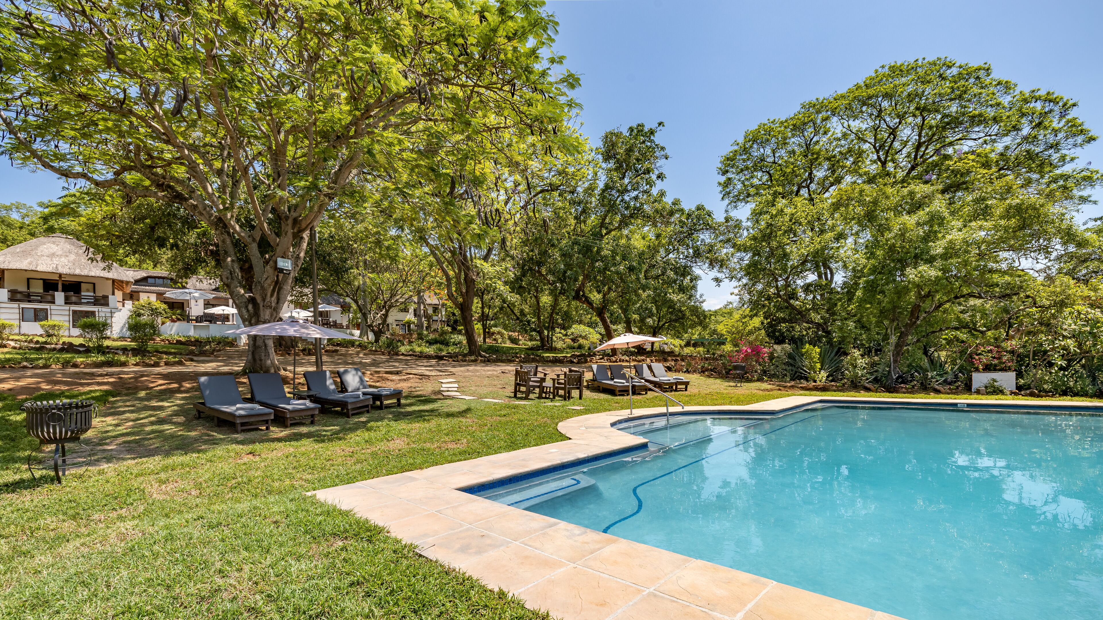 A swimming pool surrounded by grass, trees, and outdoor furniture.
