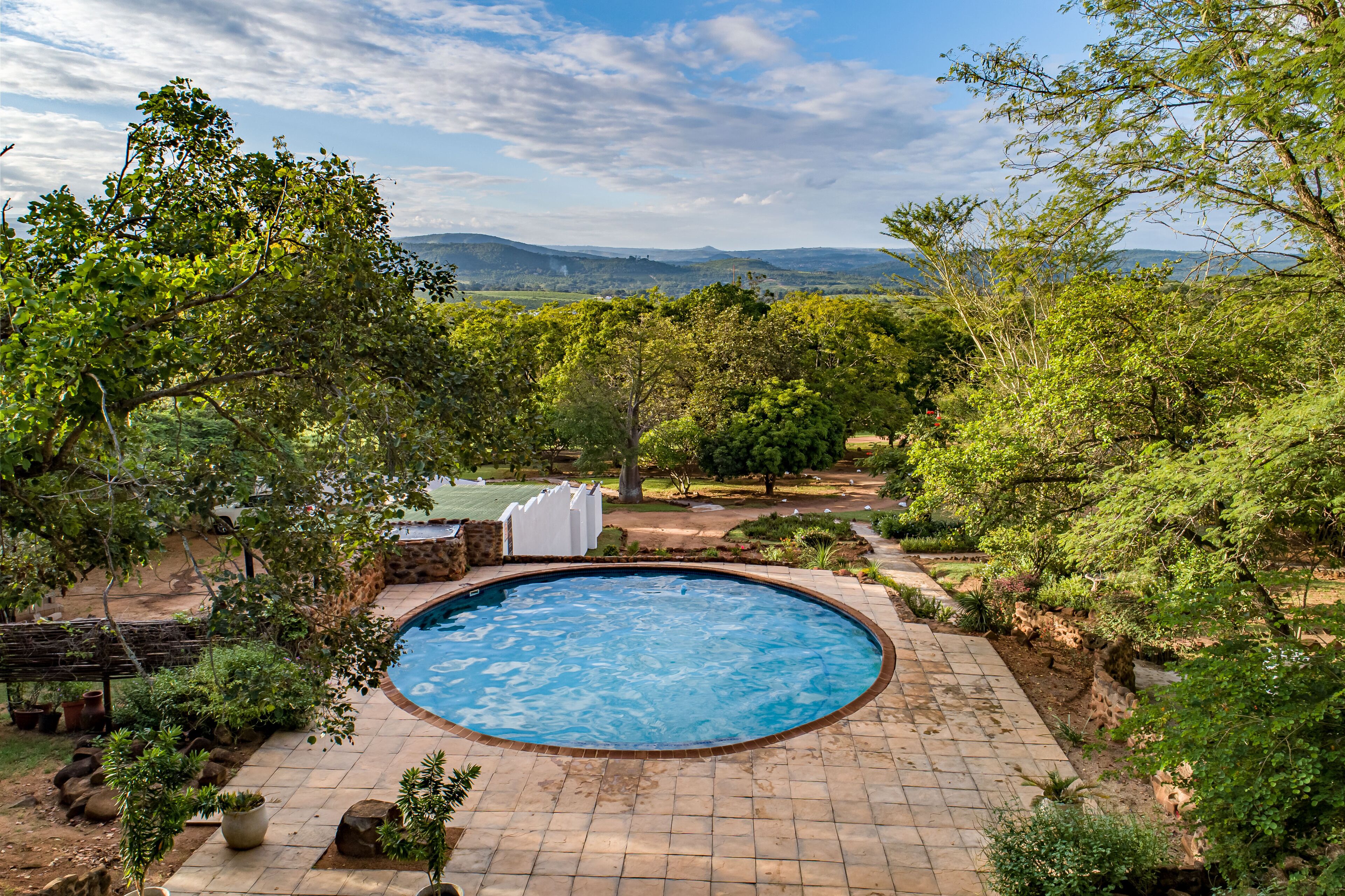 A swimming pool surrounded by lush greenery and a view of distant hills.