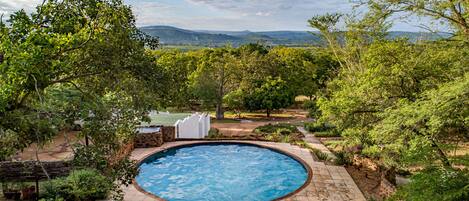 A swimming pool surrounded by lush greenery and a view of distant hills.