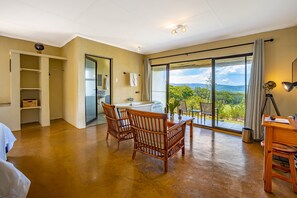 A spacious room with a large sliding glass door leading to a balcony, a white bathtub, two wicker chairs, and a wooden table.