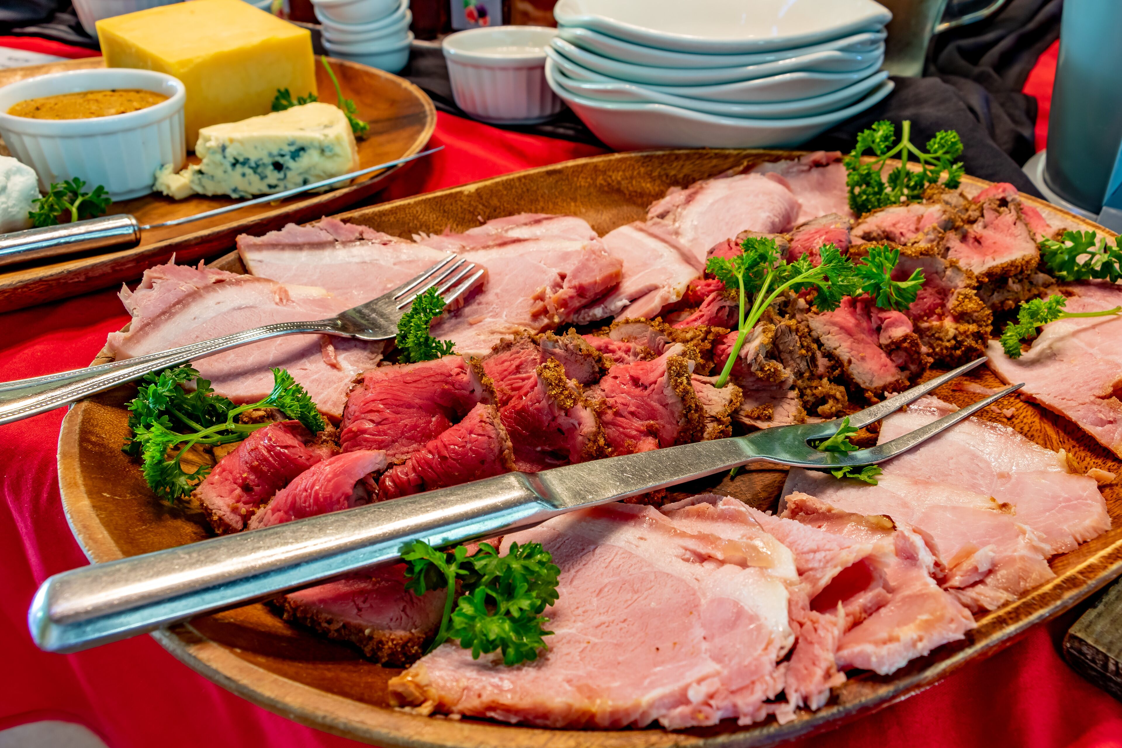 A platter of sliced meat garnished with parsley, accompanied by a cheese and a small bowl of sauce.