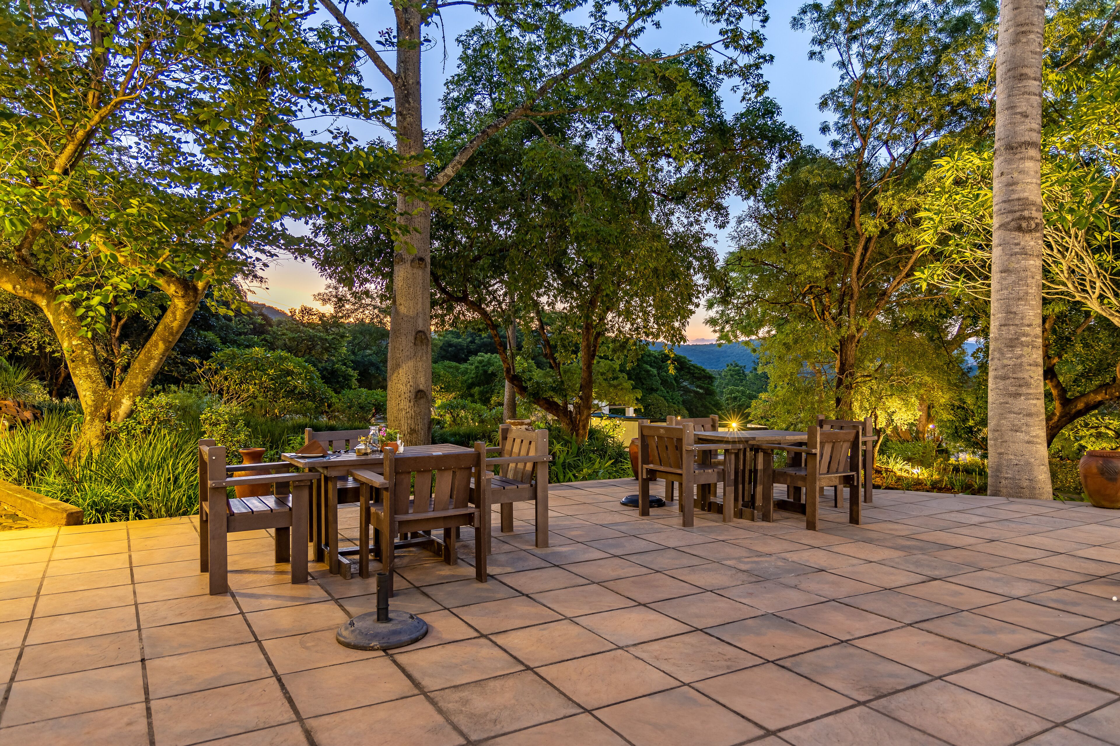 Eine Terrasse im Freien mit Holztischen und -stühlen, umgeben von Bäumen und Grünpflanzen.