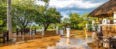 An outdoor patio with tiled flooring, wooden furniture, and a stone wall.