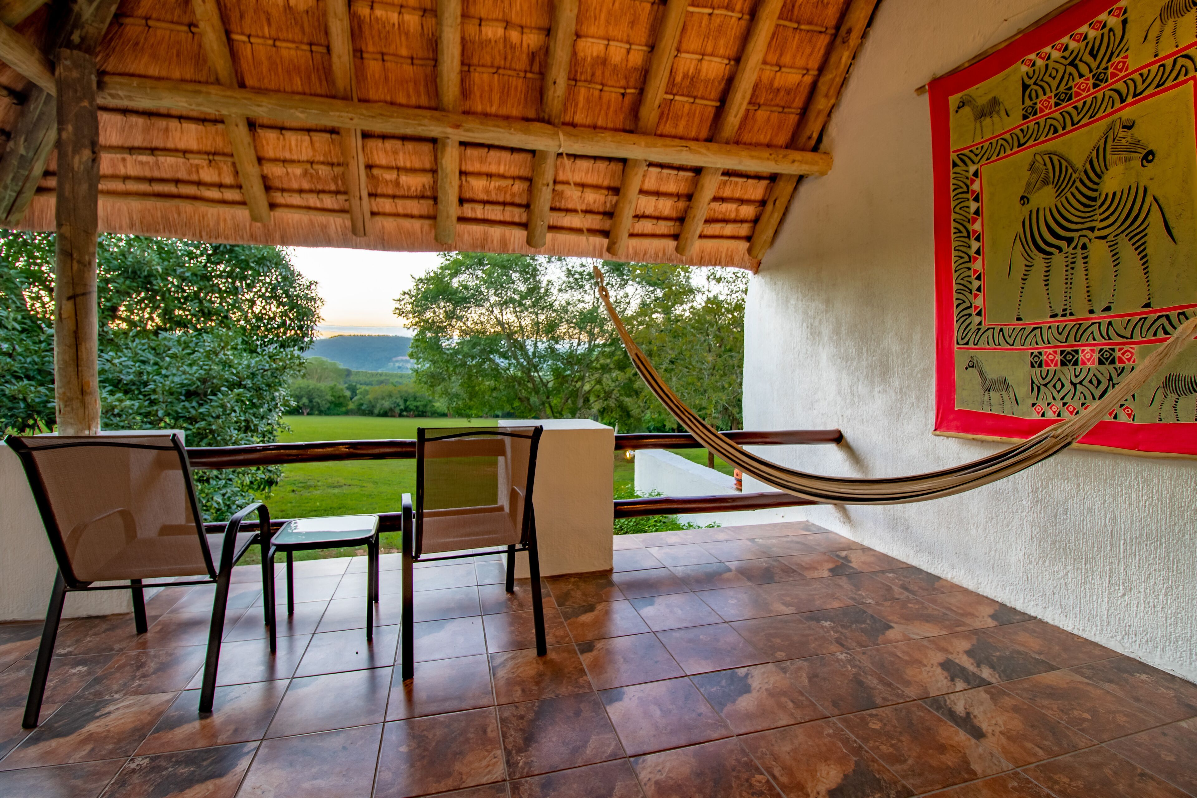 A covered outdoor area with a hammock, chairs, and a view of a green landscape.