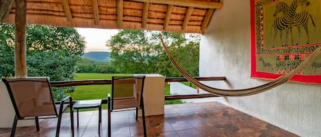 A covered outdoor area with a hammock, chairs, and a view of a green landscape.