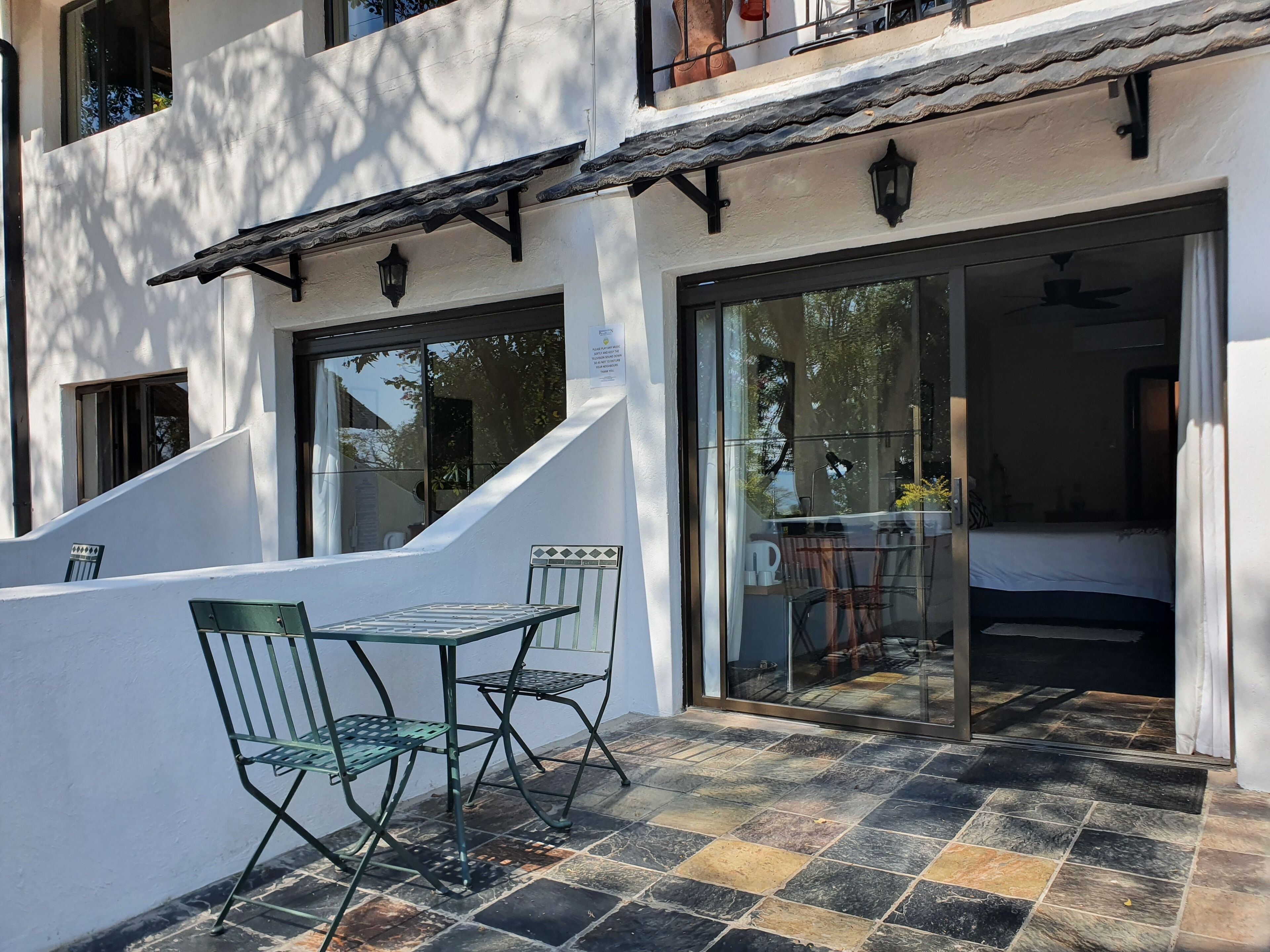 Une terrasse avec une table et des chaises, un sol carrelé et une porte vitrée donnant sur un espace intérieur.