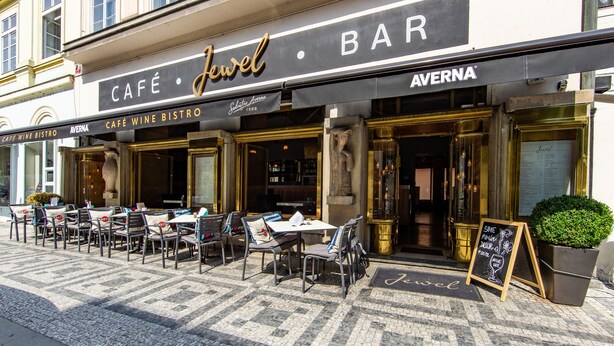 Ett utomhusområde med bord och stolar, placerat framför ett café och en bar som heter ”Jewel”.