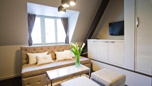 Ett modernt vardagsrum med en soffa, ett soffbord och pallar. Det finns ett fönster med gardiner, en platt-TV som är monterad på väggen och en taklampa.