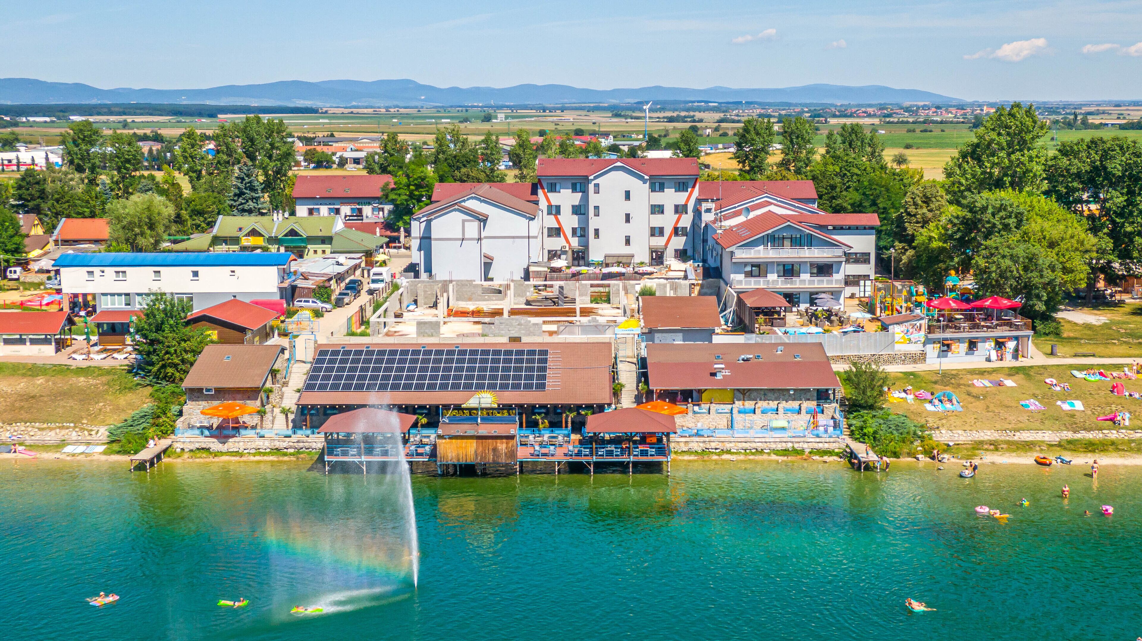 Un hotel junto al lago con varias edificaciones, una zona para nadar y una fuente.