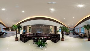 A spacious lobby with a curved seating area, a reception desk, and multiple potted plants. - Hotel Sun (Senec)
