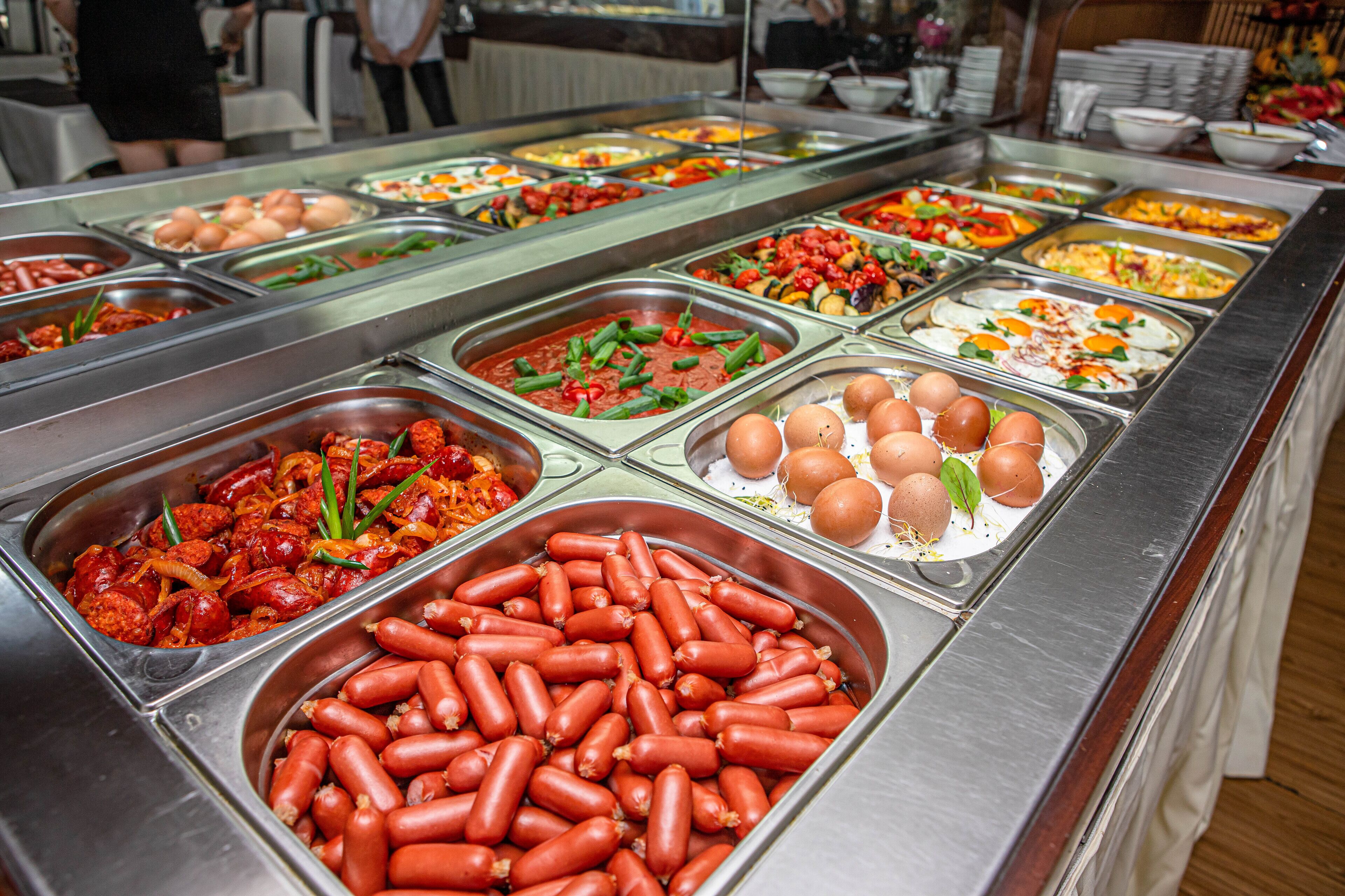 Un bufé con diversas opciones de comida, incluyendo salchichas, huevos y verduras.