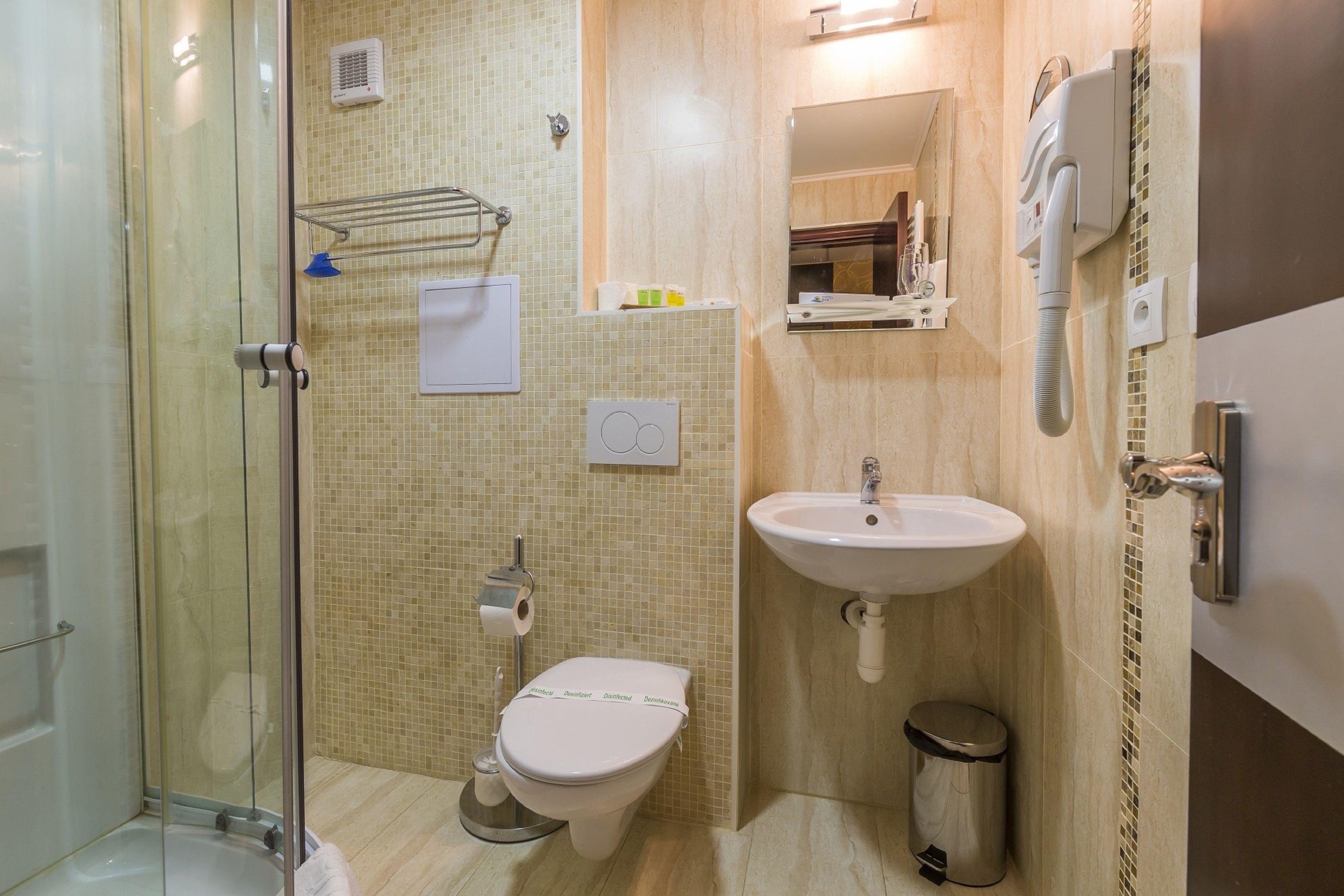 A bathroom with a glass shower enclosure, a toilet, a sink, and a trash can.