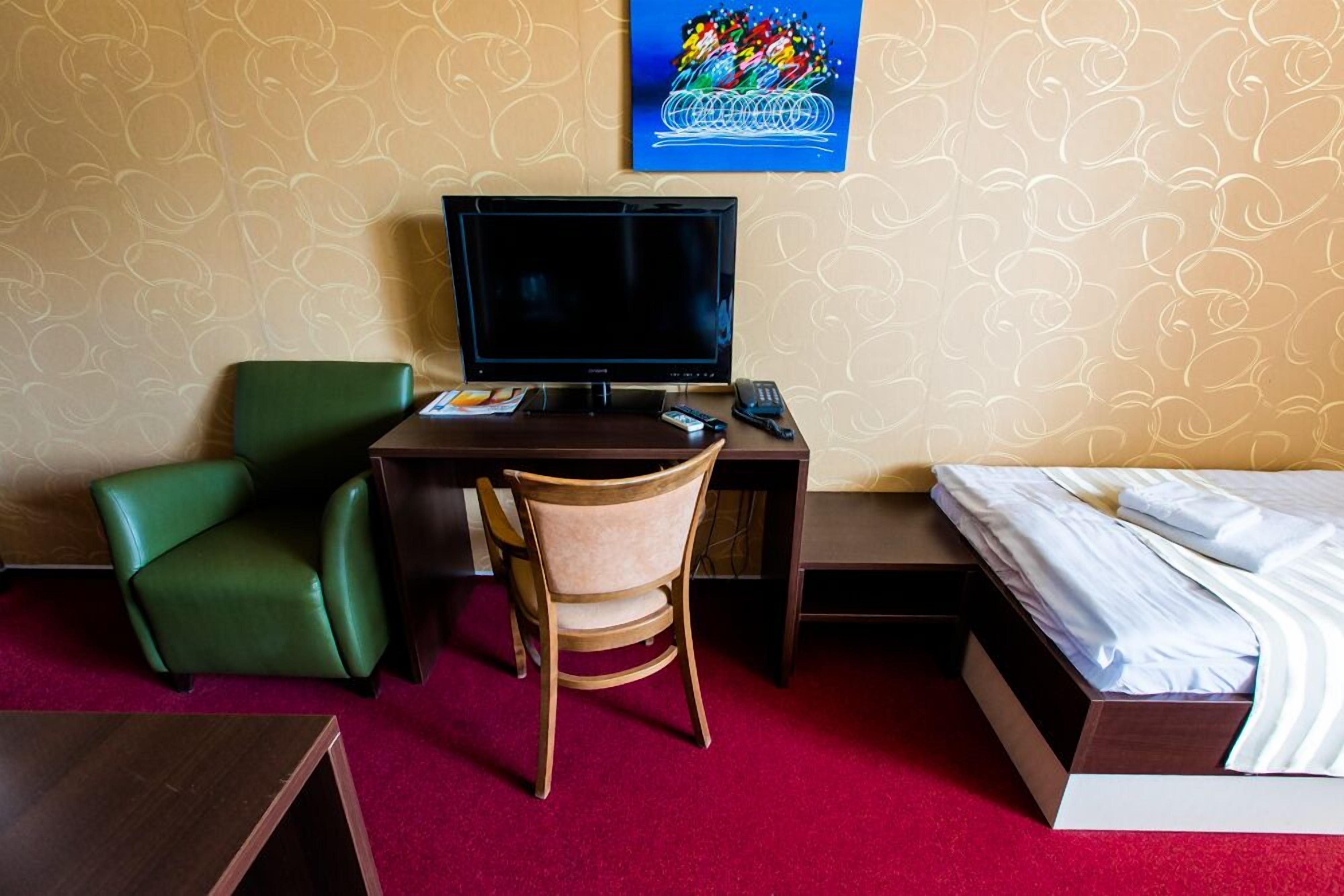Una habitación de hotel con escritorio, una silla verde, cama y televisor.