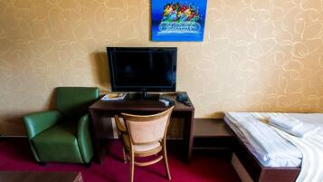 Una habitación de hotel con escritorio, una silla verde, cama y televisor.