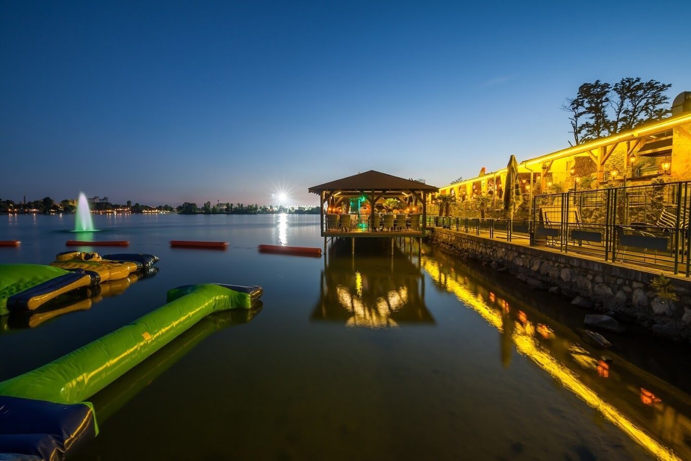 A waterfront area with a covered seating area, inflatable rafts, and a building with outdoor seating.