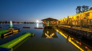 A waterfront area with a covered seating area, inflatable rafts, and a building with outdoor seating.