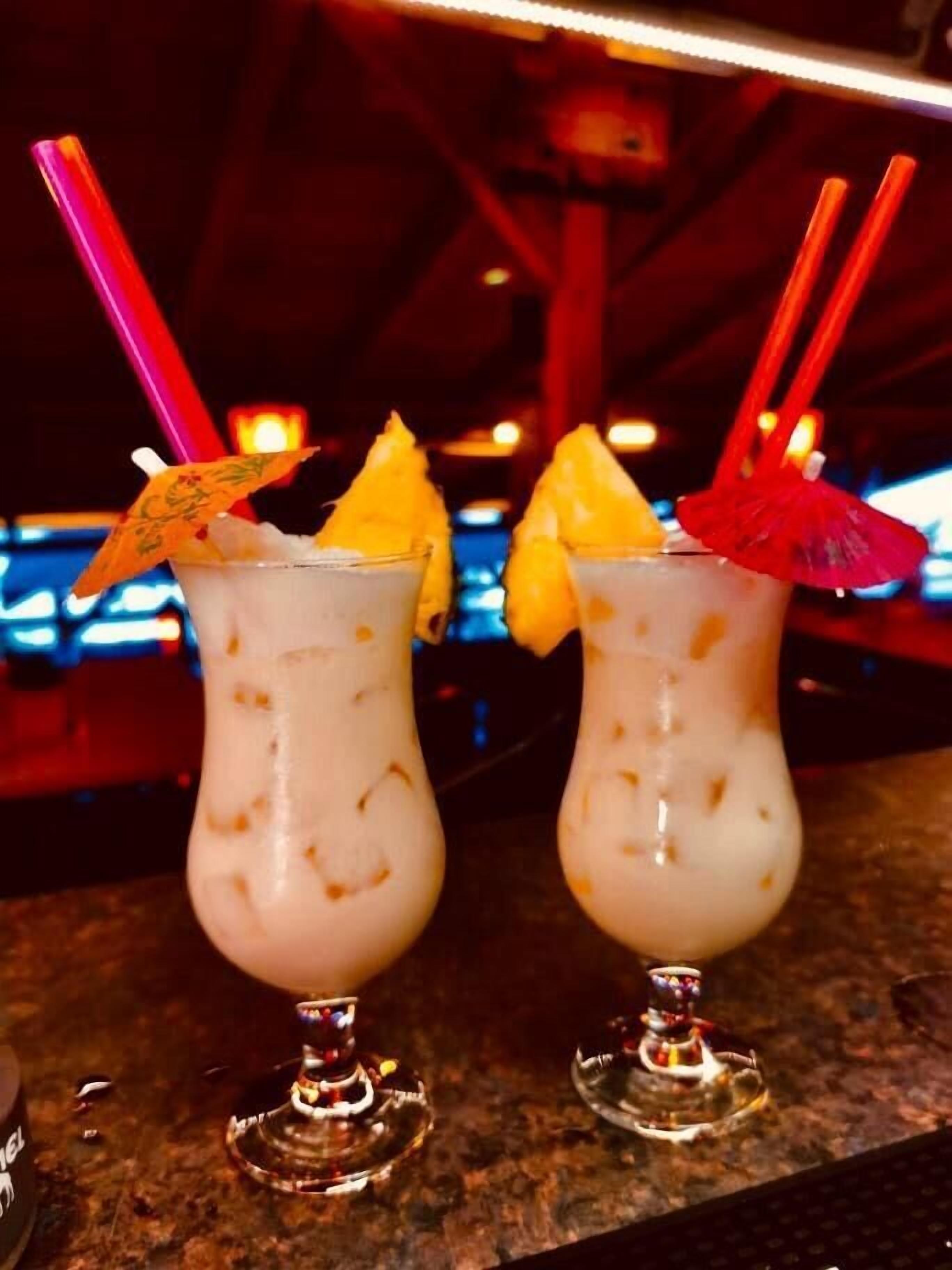 Due cocktail con guarnizioni di frutta e cannucce, serviti in bicchieri con un ombrello decorativo.