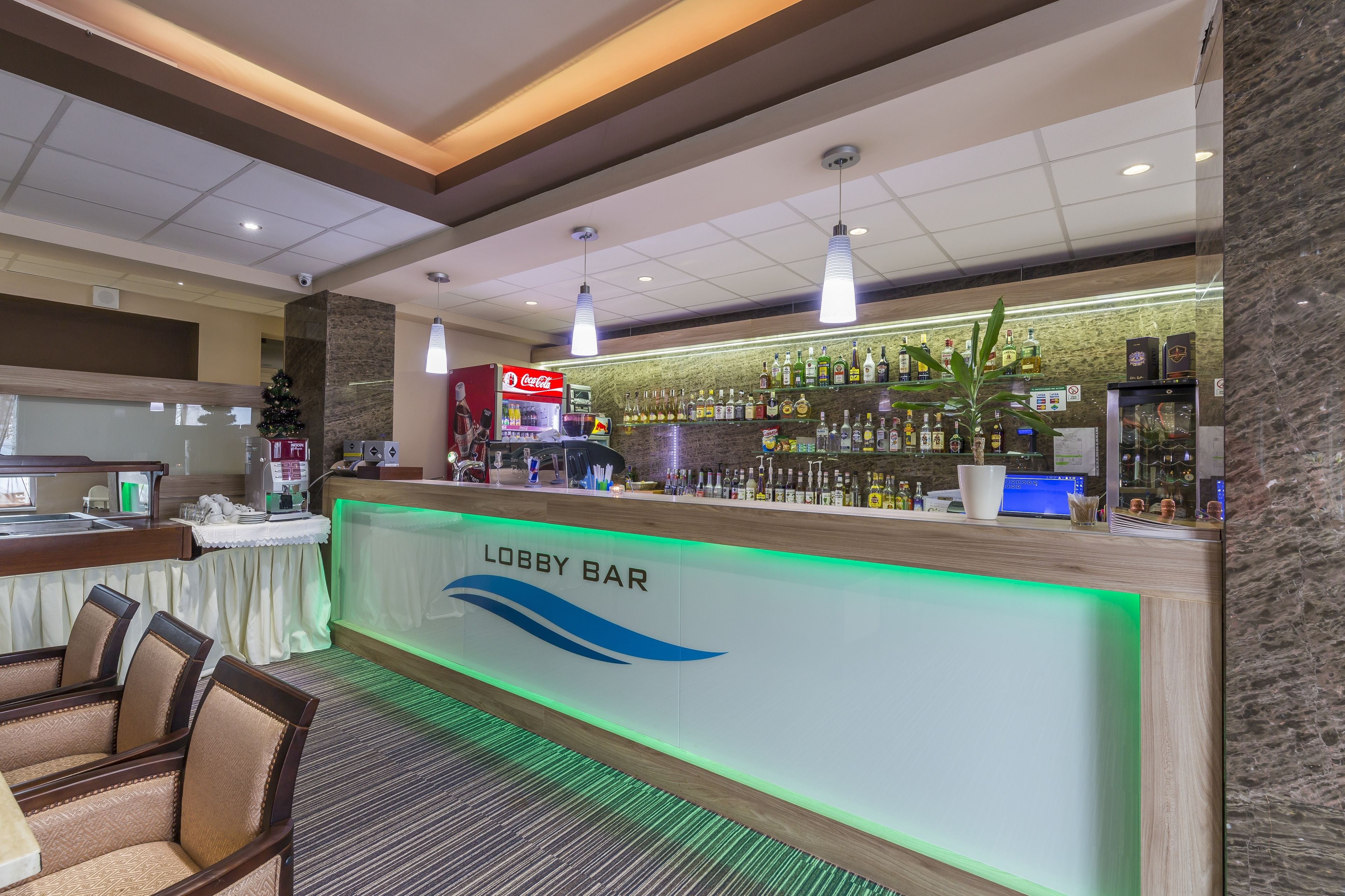 Un bar nella hall con reception, area relax e una parete di bottiglie di liquori.