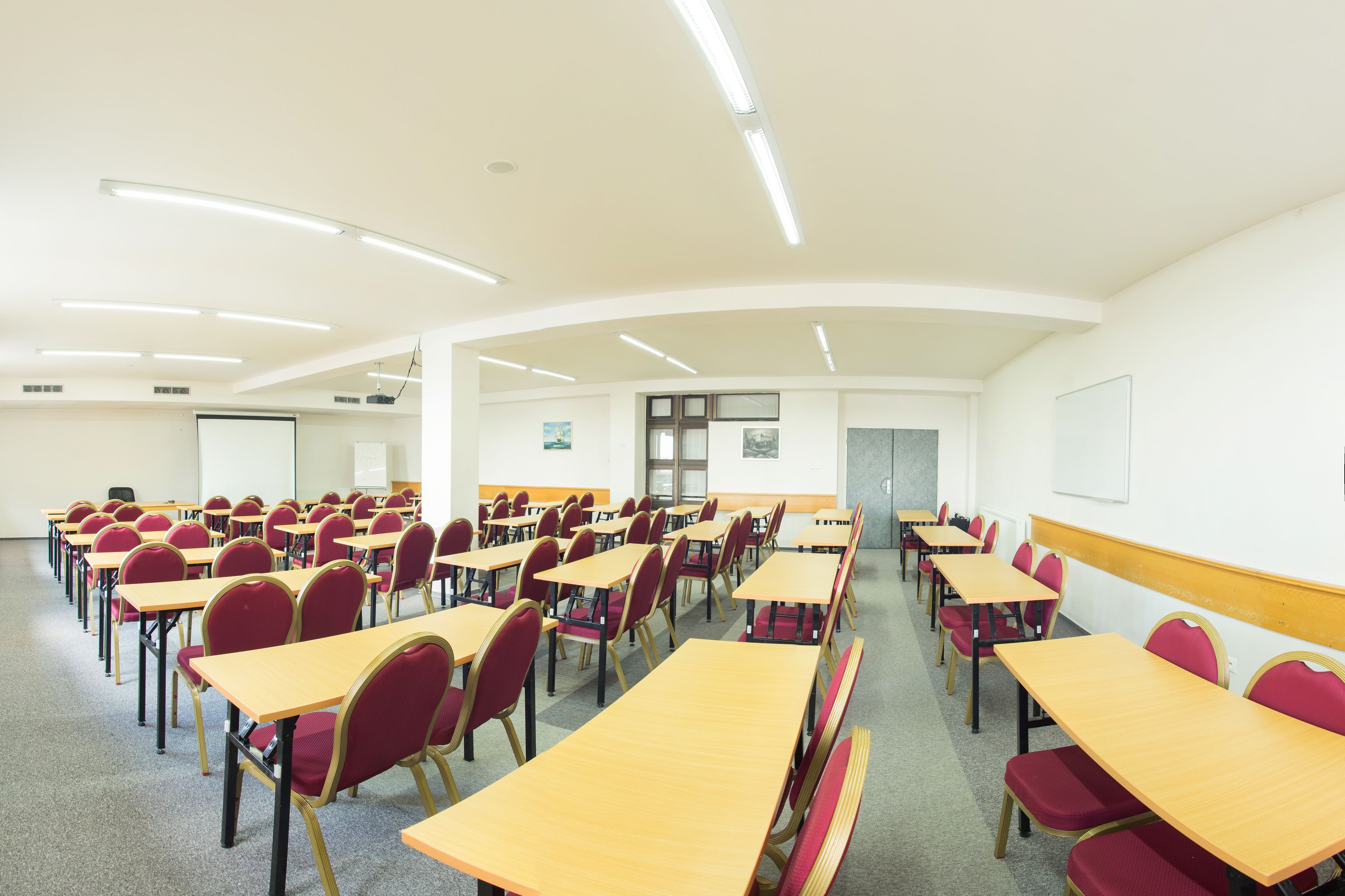 A classroom with rows of desks and chairs, a projector screen, and a whiteboard.