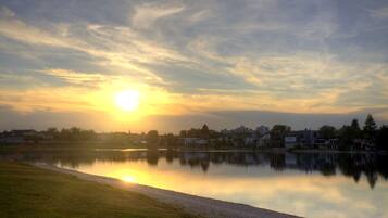 Un lago tranquilo reflejando el atardecer, con una hilera de casas al fondo.