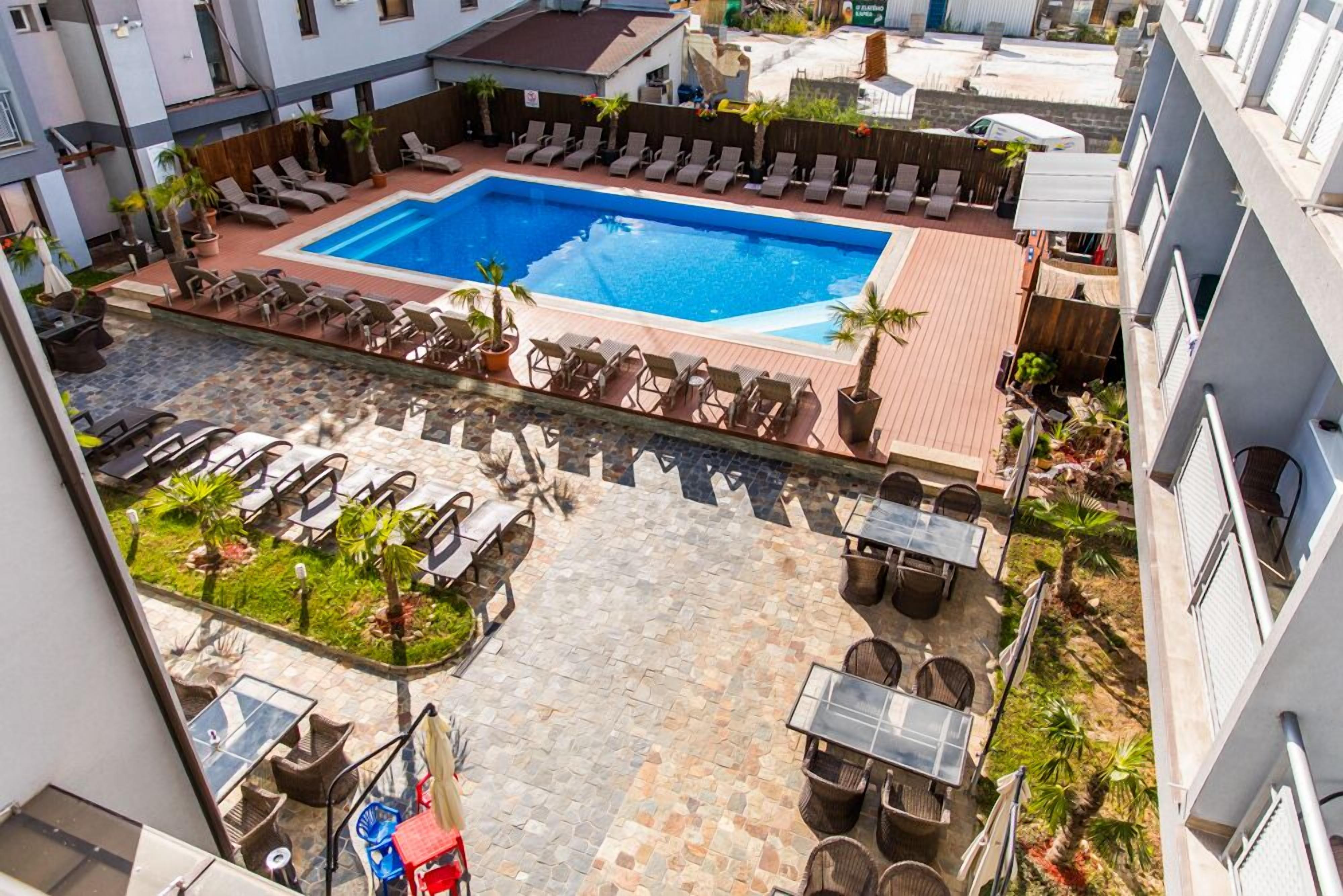 A rooftop pool area with lounge chairs, a dining area, and a small garden.