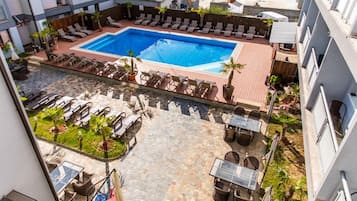 A rooftop pool area with lounge chairs, a dining area, and a small garden.