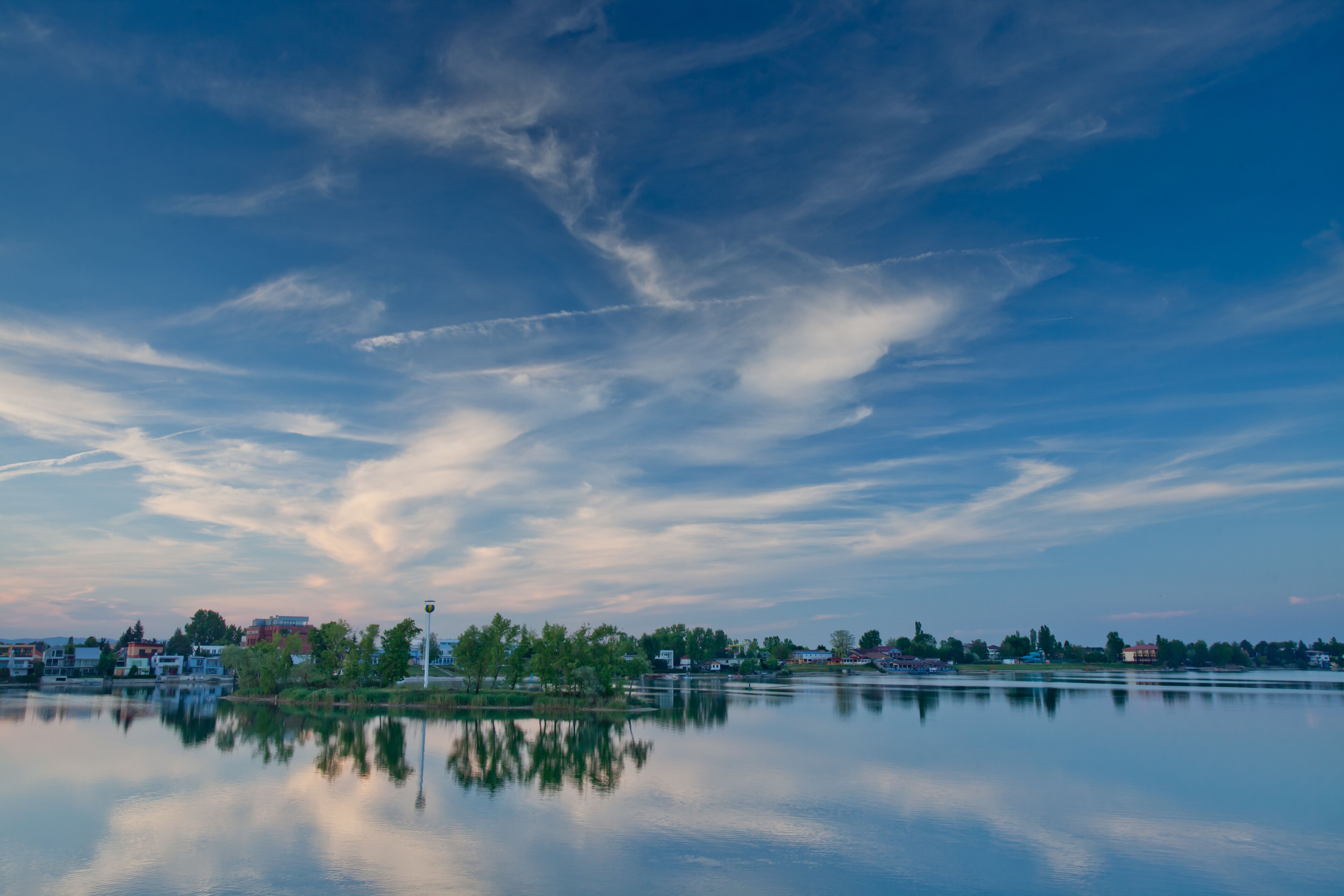 A calm lake with a clear reflection of the sky and buildings.