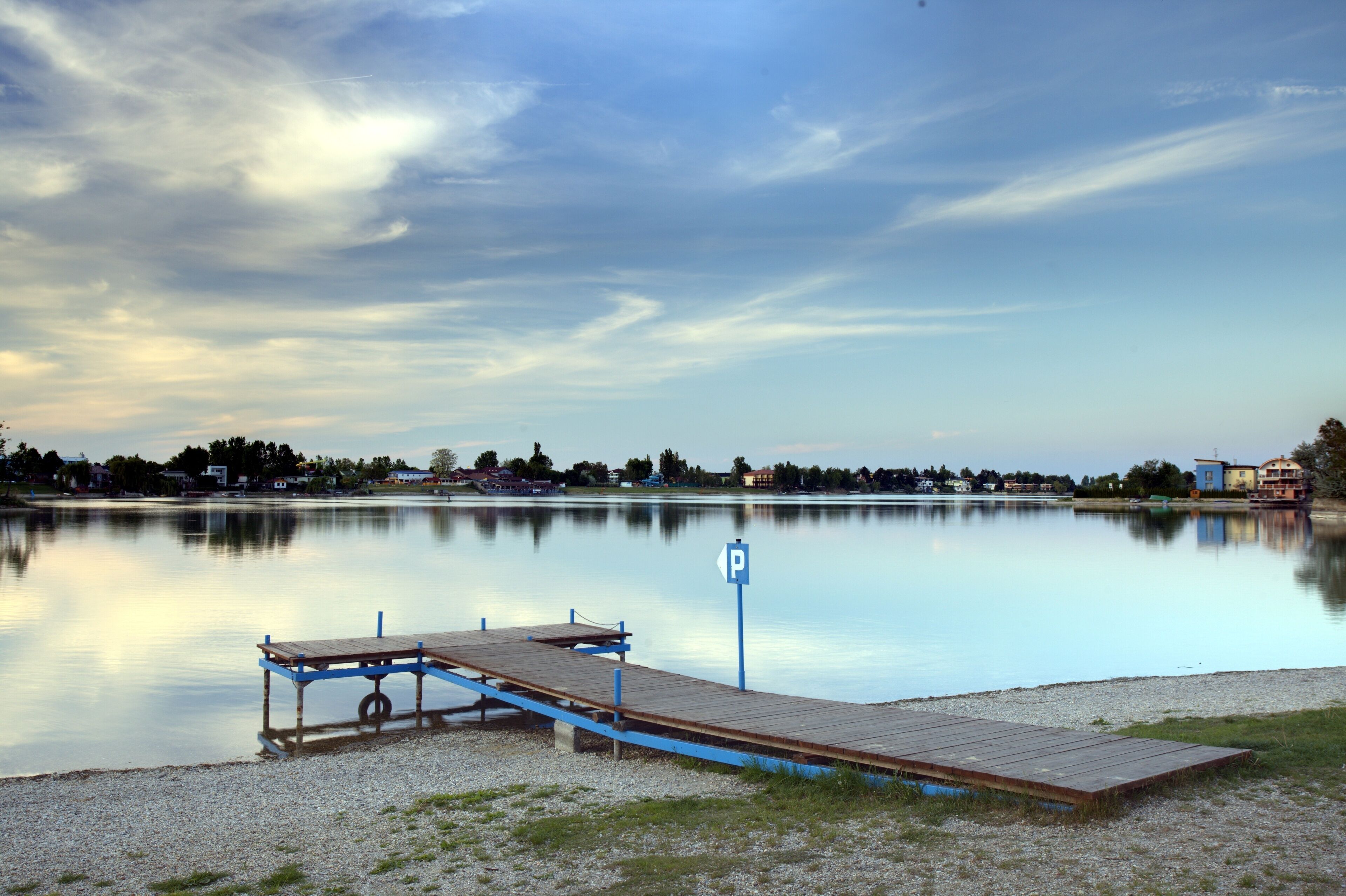 Un lago tranquilo con un muelle de madera y una señal de estacionamiento.