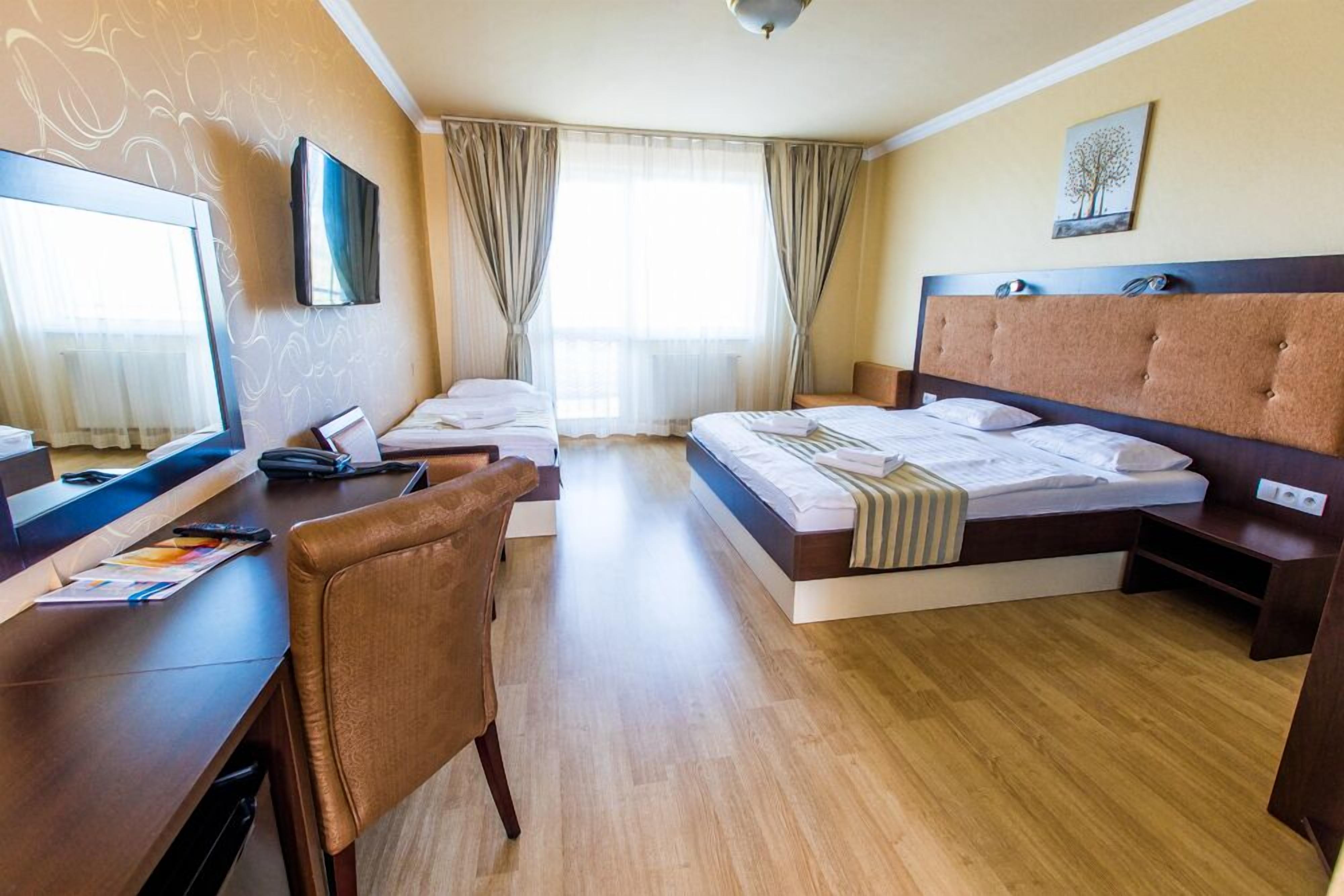 A hotel room with a bed, a desk with a chair, a television, and a window with curtains.