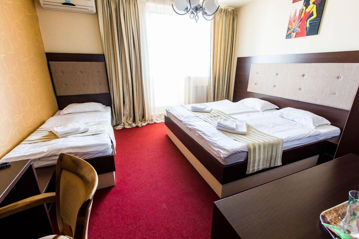 A hotel room with two single beds, a desk, a chair, and a dining table.