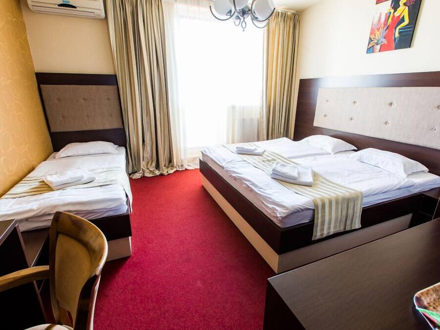 A hotel room with two single beds, a desk, a chair, and a dining table.