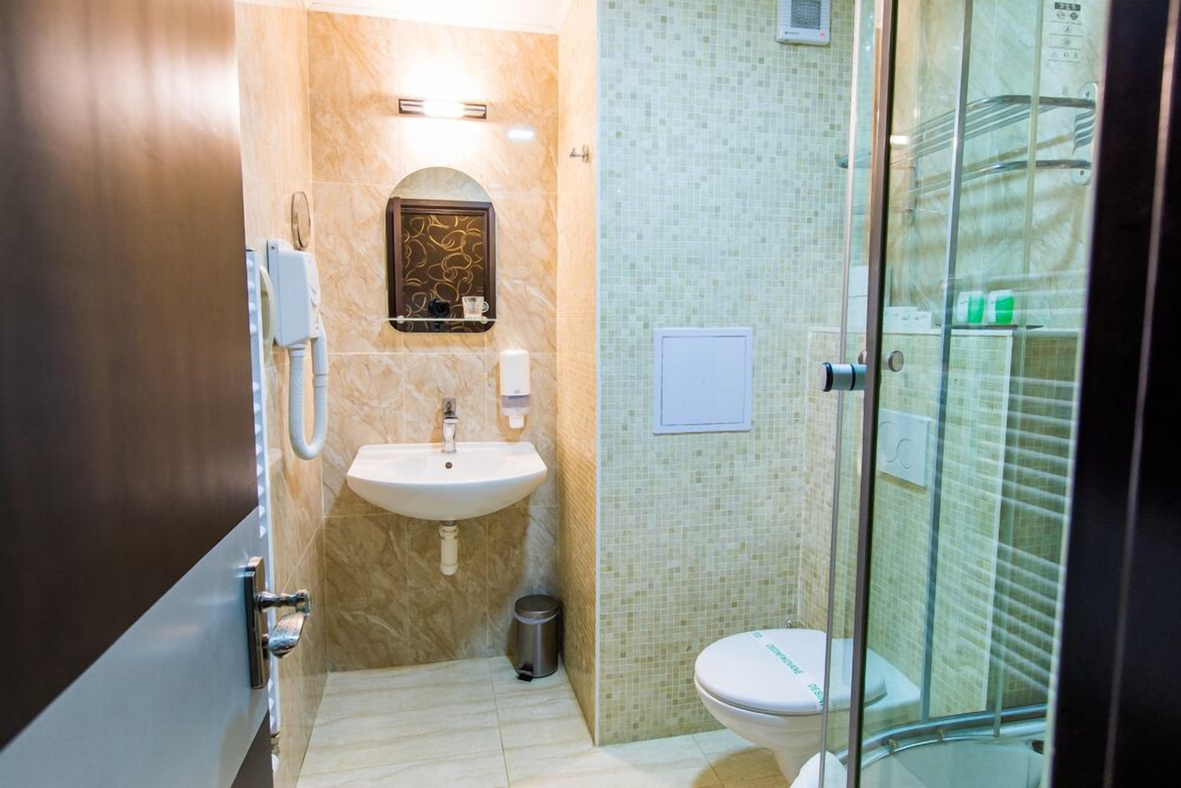 A compact bathroom with a sink, toilet, and glass-enclosed shower stall.