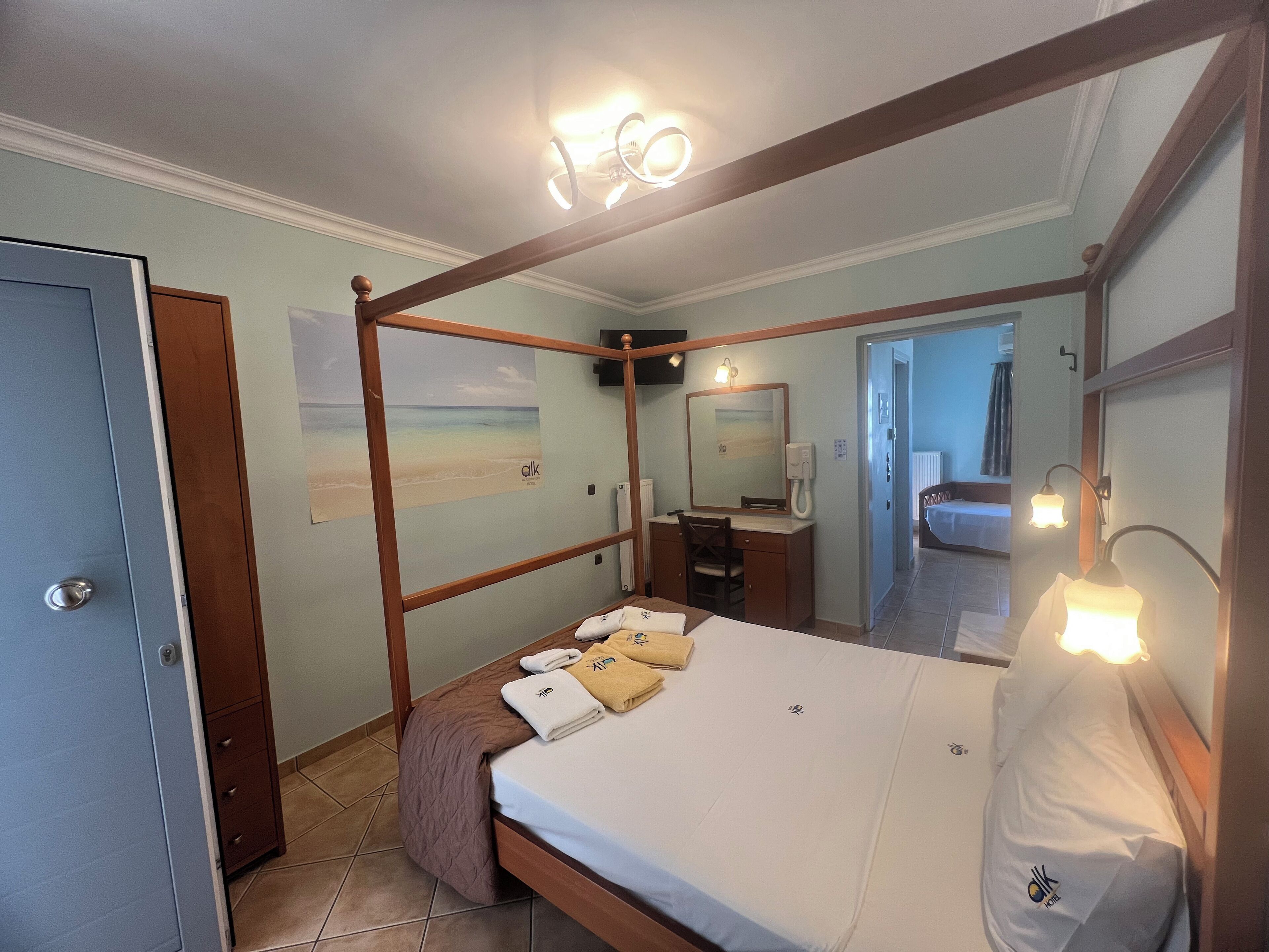 Un lit à baldaquin avec un cadre en bois, une table de chevet, un miroir et un luminaire fixé au mur.
