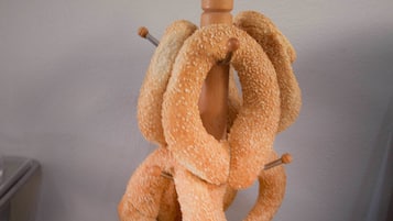 Een houten standaard met een brood in de vorm van een lus, bedekt met sesamzaad.