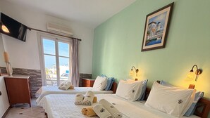 Habitación de hotel con dos camas, un escritorio, una silla, un ventanal con cortinas, un cuadro en la pared y suelo de baldosas.