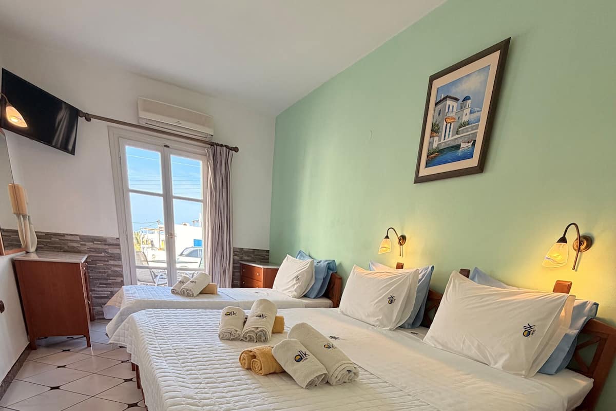 Ein Hotelzimmer mit zwei Betten, einem Schreibtisch, einem Stuhl, einem Fenster mit Vorhängen, einem Bild an der Wand und einem Fliesenboden.