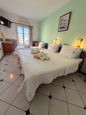 Habitación de hotel con dos camas, un escritorio, una silla, un ventanal con cortinas, un cuadro en la pared y suelo de baldosas.