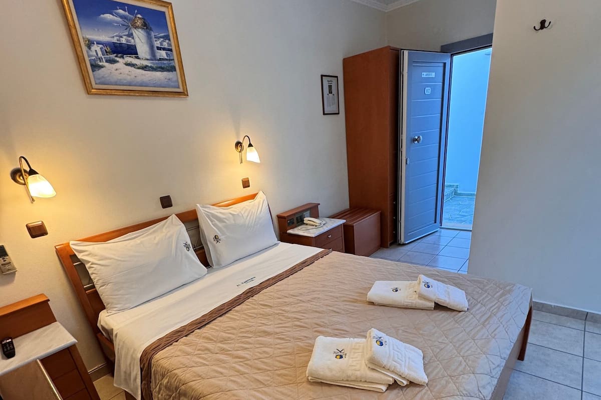 Ein Hotelzimmer mit Bett, Nachttischen, einem Bild, einer Wandleuchte und Blick ins Freie.